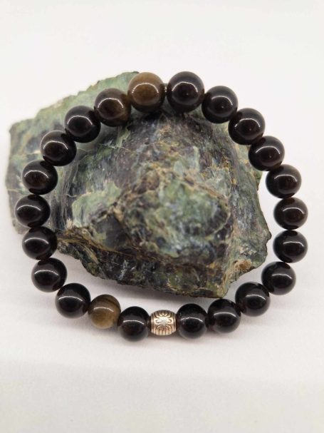Bracelet en perles noires avec une perle translucide, posé sur une roche.