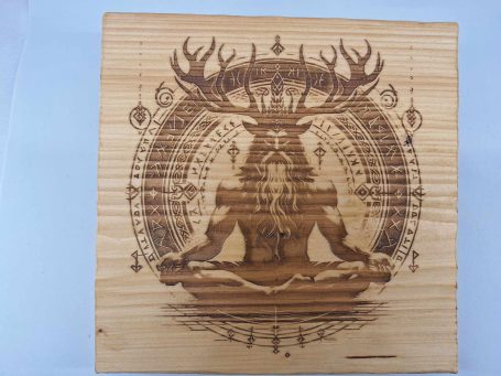 Symbole spirituel gravé sur bois représentant un être à cornes en méditation.
